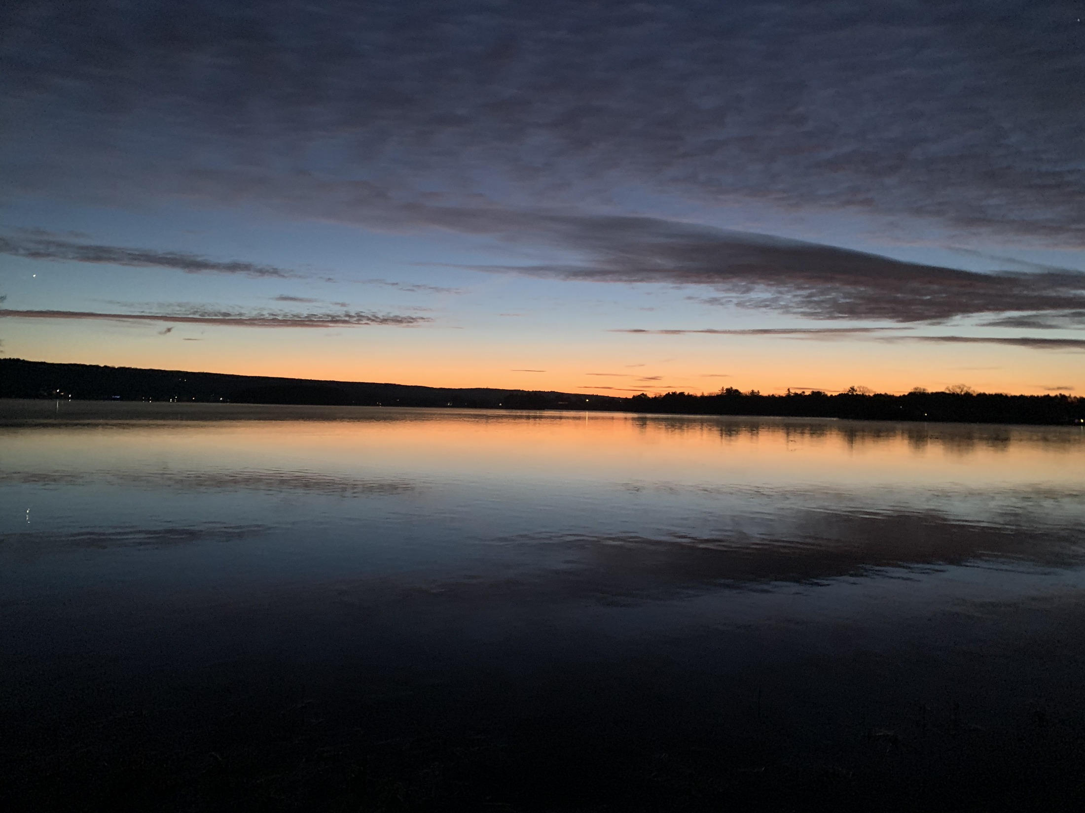 Sunset over Webster Lake with still water reflecting a dark cloud shelf and bright horizon.